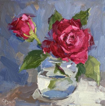 Red roses in clear glass vase against a blue grey backround